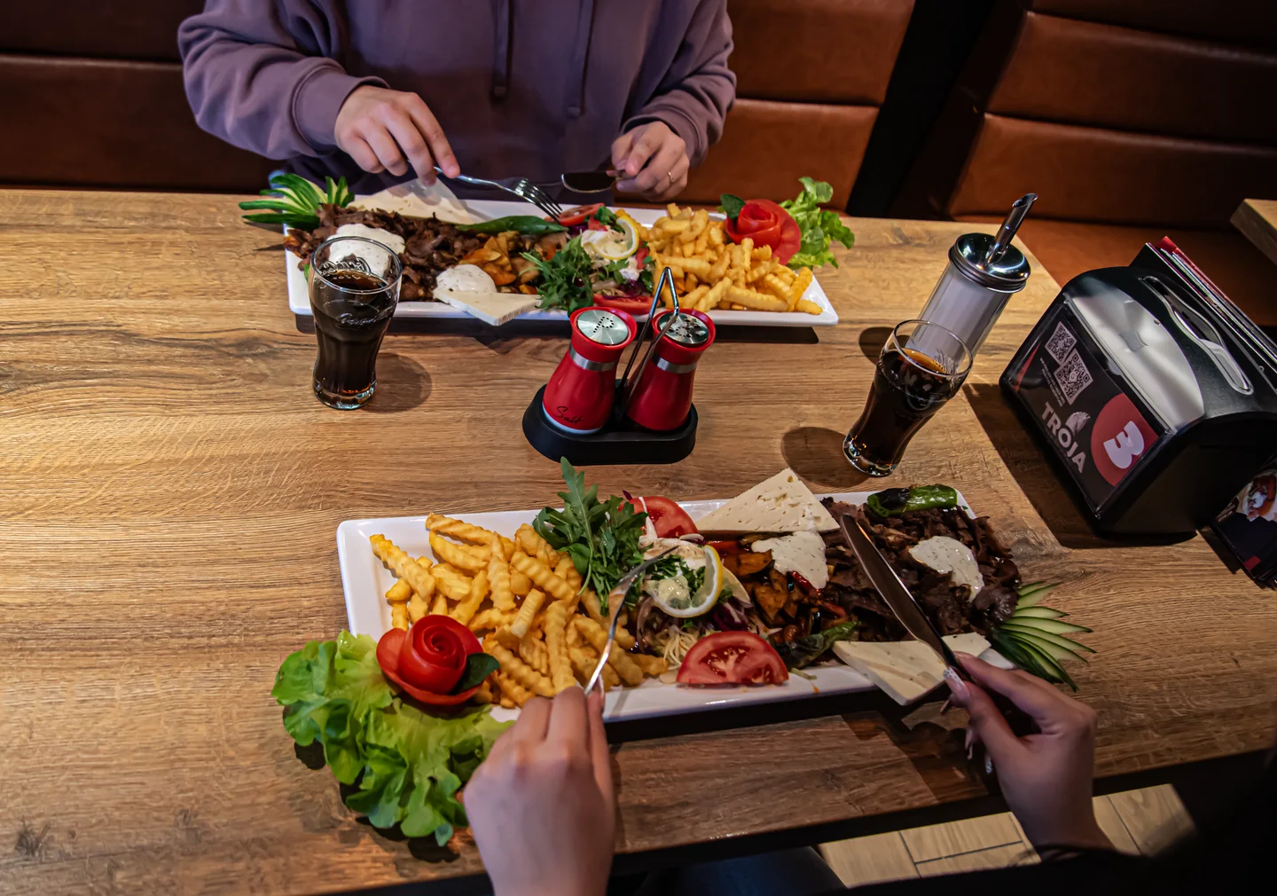 Zwei Tellergerichte mit Fleisch, Pommes und Salat auf einem Holztisch bei Troja.